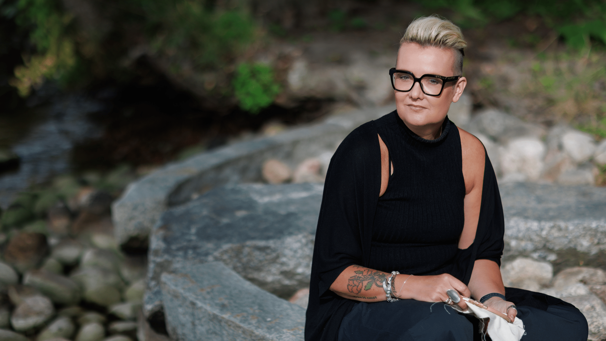 Henkilö mustassa asussa, pitelee ristipistotyötä käsissään
