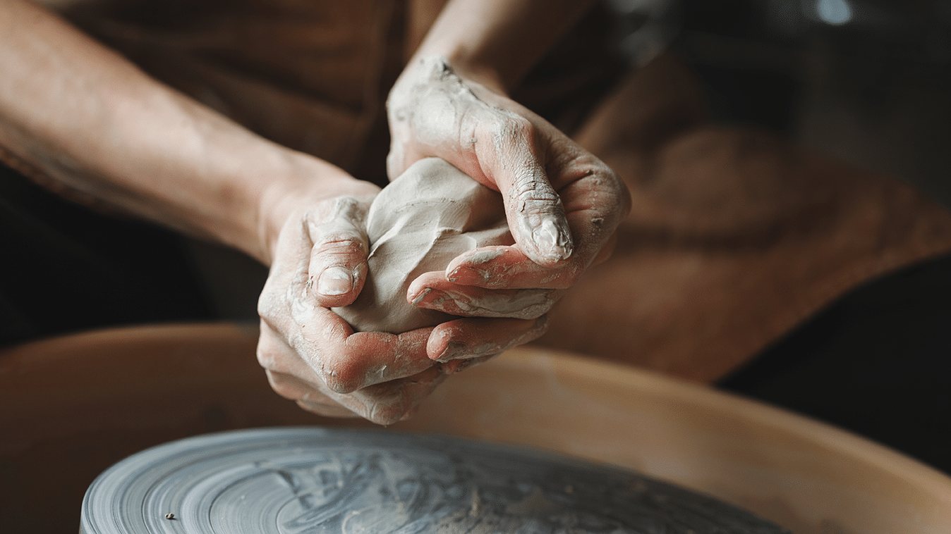 Lähikuva käsistä, jotka työstävät savenpalaa, alla näkyy dreija.