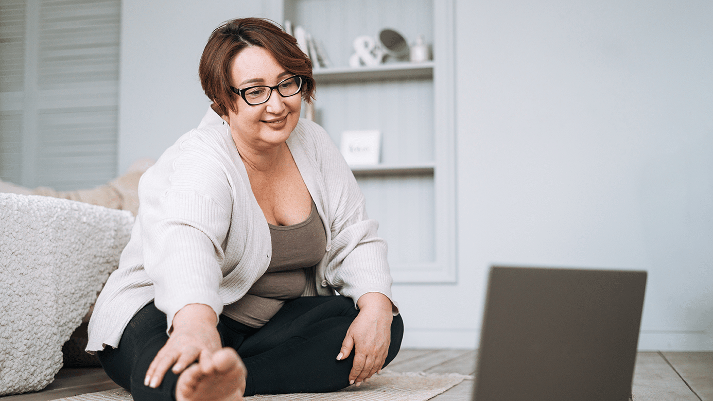 Henkilö tekee venytystä kotona lattialla, edessä on läppäri avoinna.