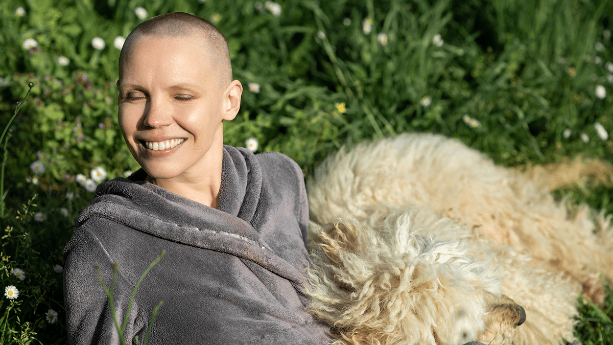 Hymyilevä, lähes kalju henkilö makaa nurmikolla, hänen vieressään on vaaleaturkkinen koira