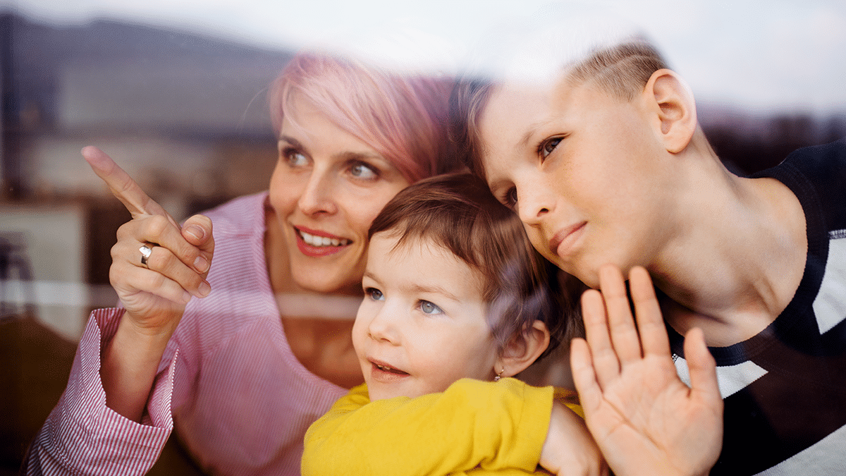Henkilö ja kaksi lasta ikkunan takana, kaikki katsovat samaan suuntaan